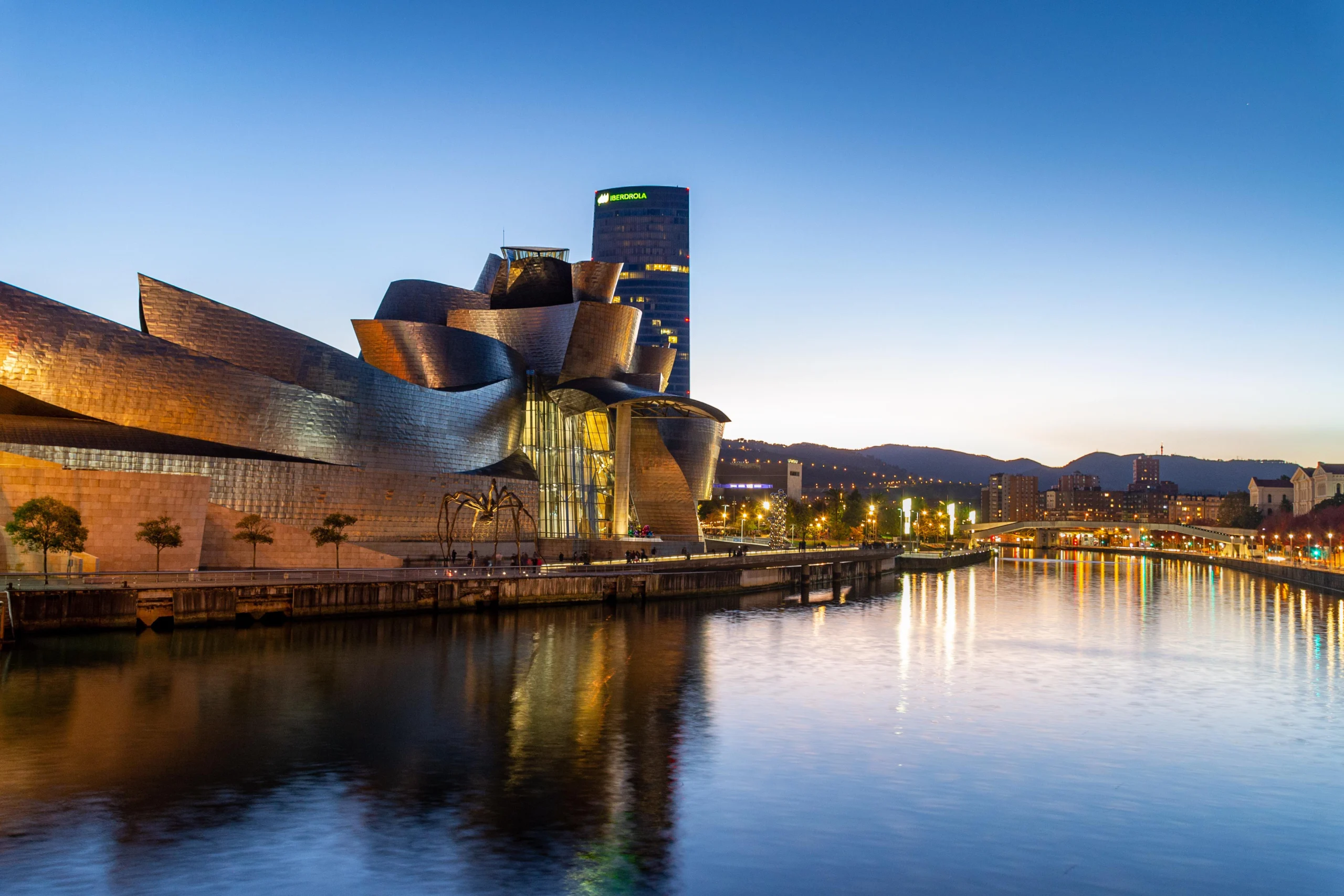 Guggenheim Museum Bilbao at dusk beside the Nervión River with city lights and reflections in Spain.