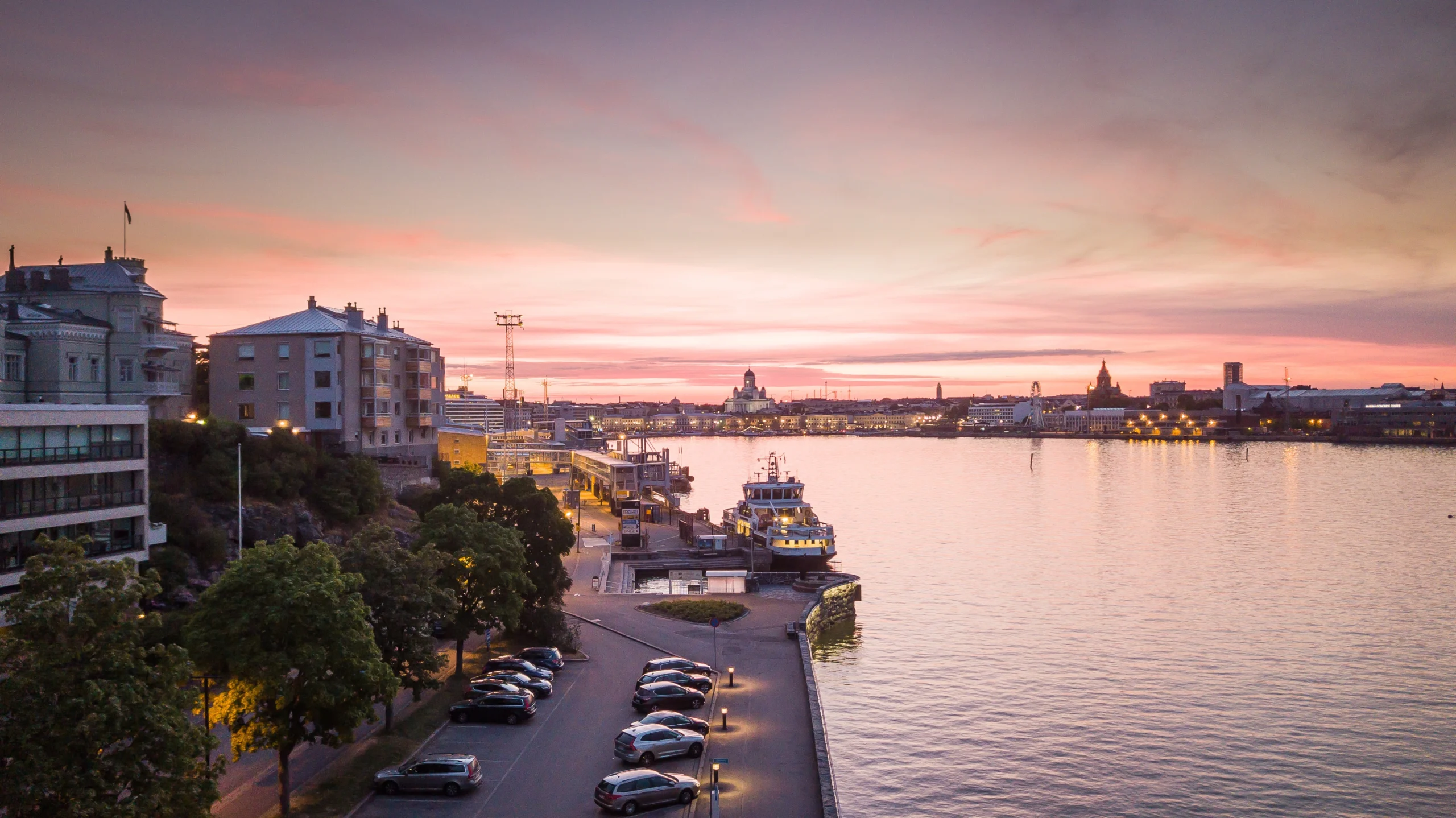 Helsinki waterfront at sunset in Finland, with ferries, calm water, city buildings, and the skyline across the harbor.