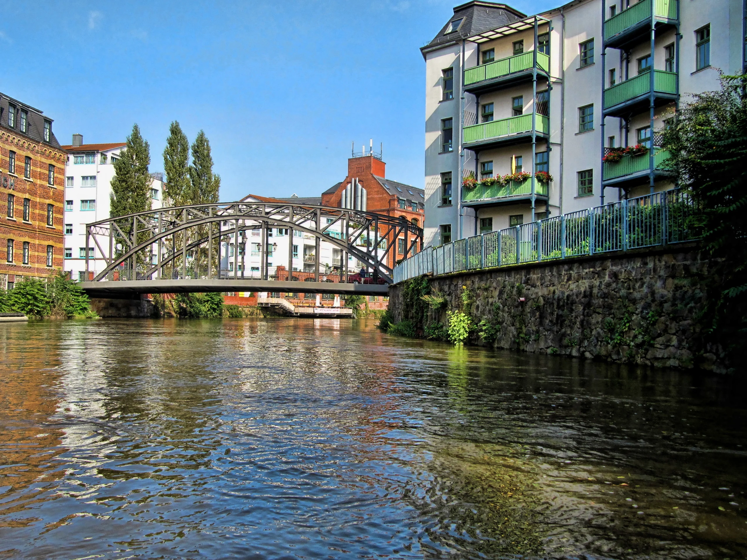 Canal and pedestrian bridge in Leipzig, Germany, with residential buildings, water, and a neighborhood streetscape.